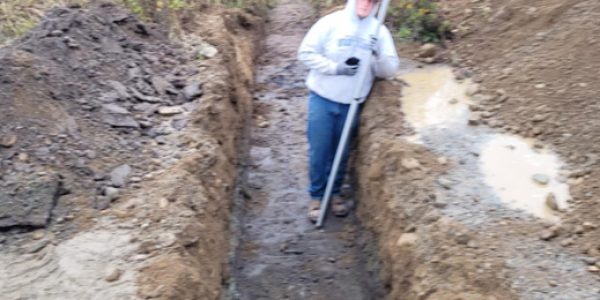 Excavator digging and leveling a trench for culvert placement on a gravel driveway in Spirit Lake